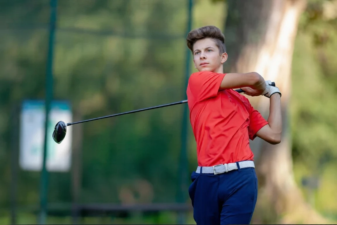 Young golfer in red shirt swinging a golf club outdoors.